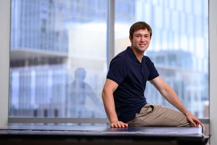 James Simon smiles while sitting on a ping pong table, with windows in background.