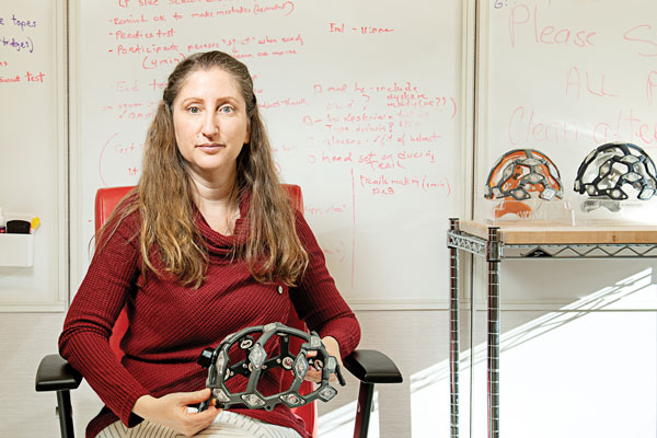 Michal Tal smiles while seated and holding a helmet-sensor device in her hands.