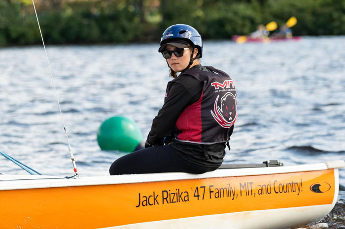 Brooke Schmelz is relaxed on a sailboat, wearing helmet and MIT Engineers life jacket